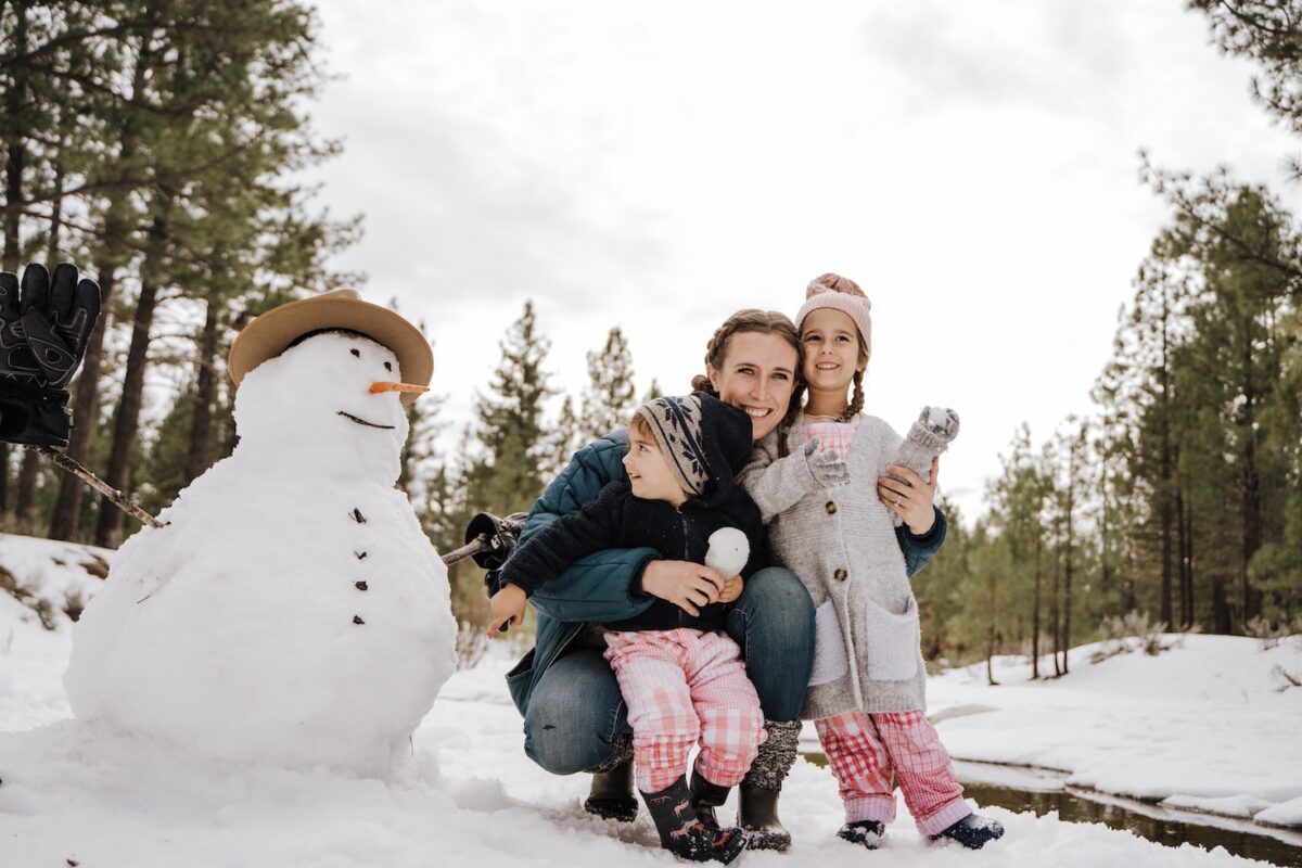 une femme et ses enfants réalisant un bonhomme de neige en hiver